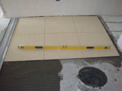 De tegel wordt met een tegellijm op een cementdekvloer gelegd