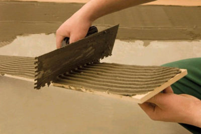 Glue is applied both to the tile and to the floor for better adhesion and to prevent voids