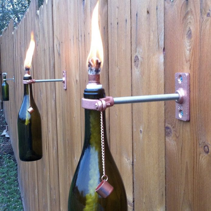 Aliejinės lempos iš butelių ant šalies tvoros